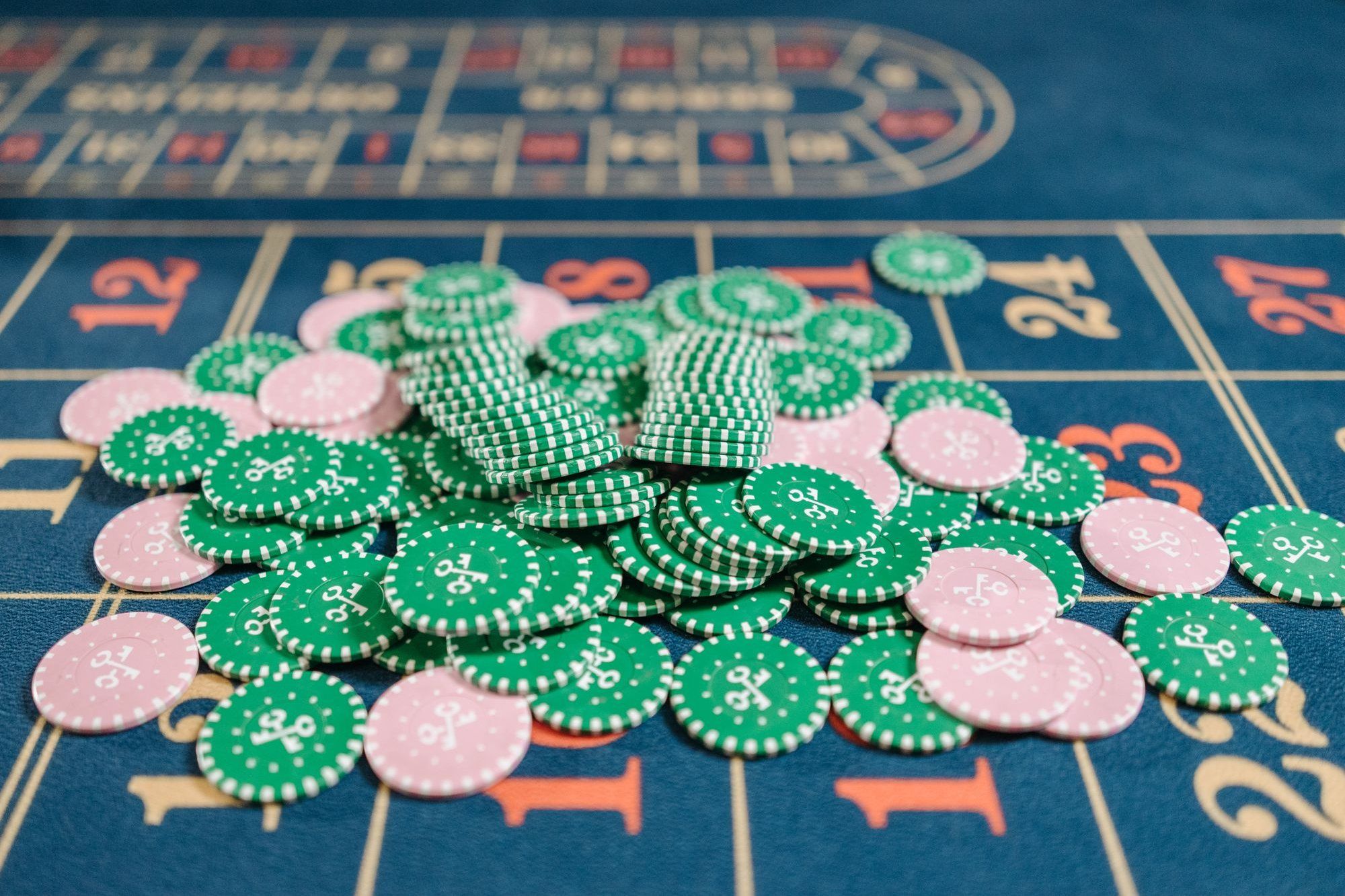 Pile of green and pink chips on a blue roulette table layout